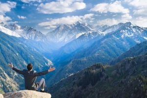Image of a young businessman who sits on the top of the mountain on the background of the beautiful mountains and relaxing